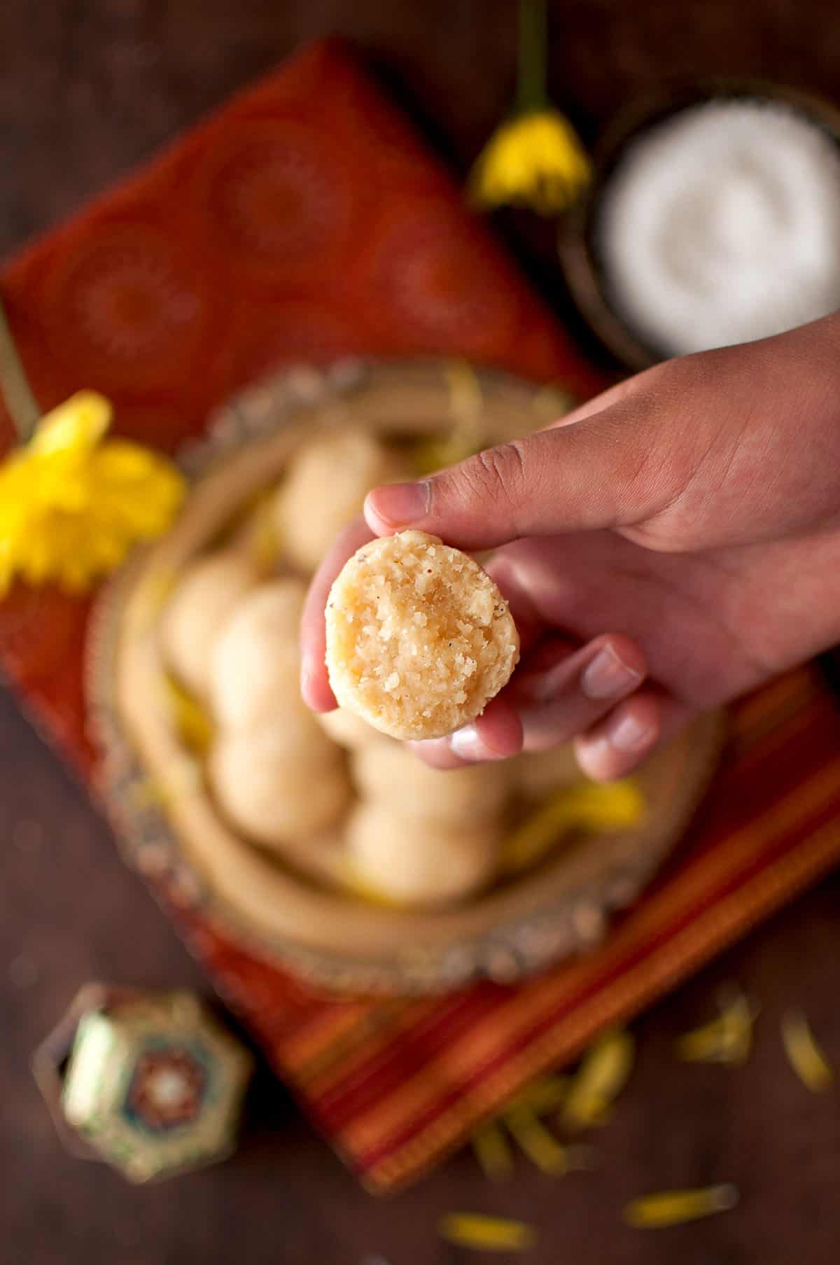 Hand holding half a coconut ladoo.