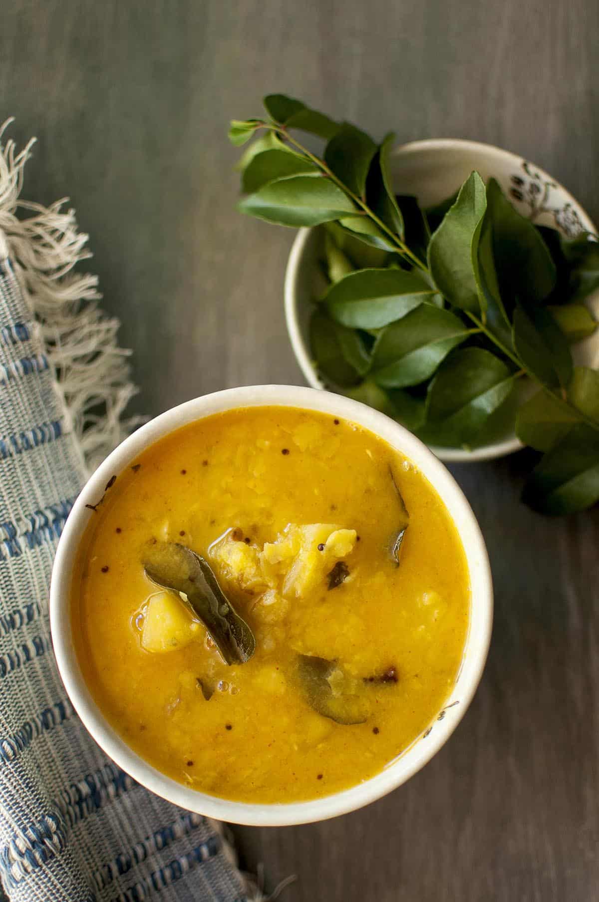 White bowl with mango dal and a sprig of curry leaves in the back