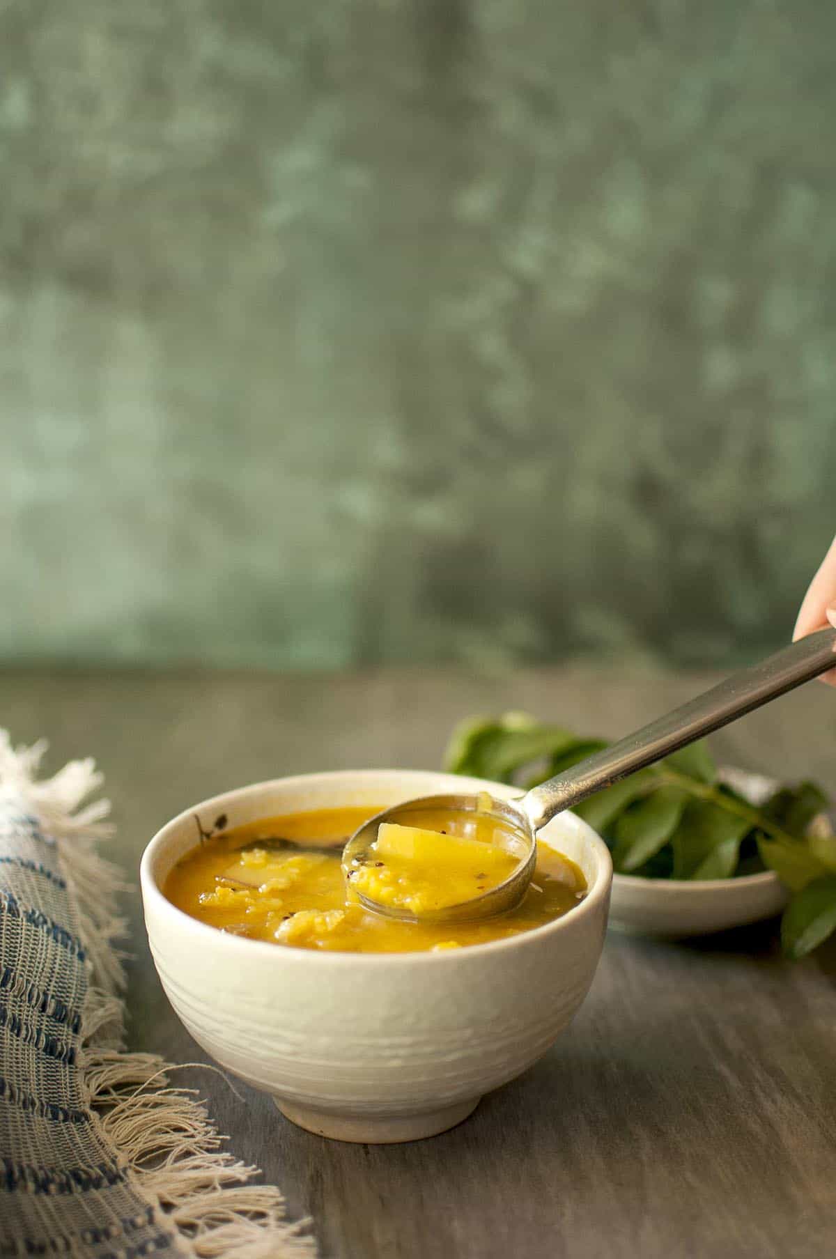 white bowl with mamidikaya pappu with a steel ladle inside