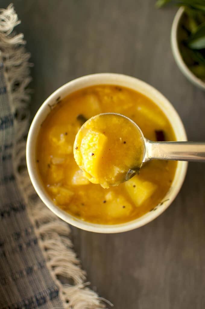 white bowl with raw mango dal with a steel ladle inside