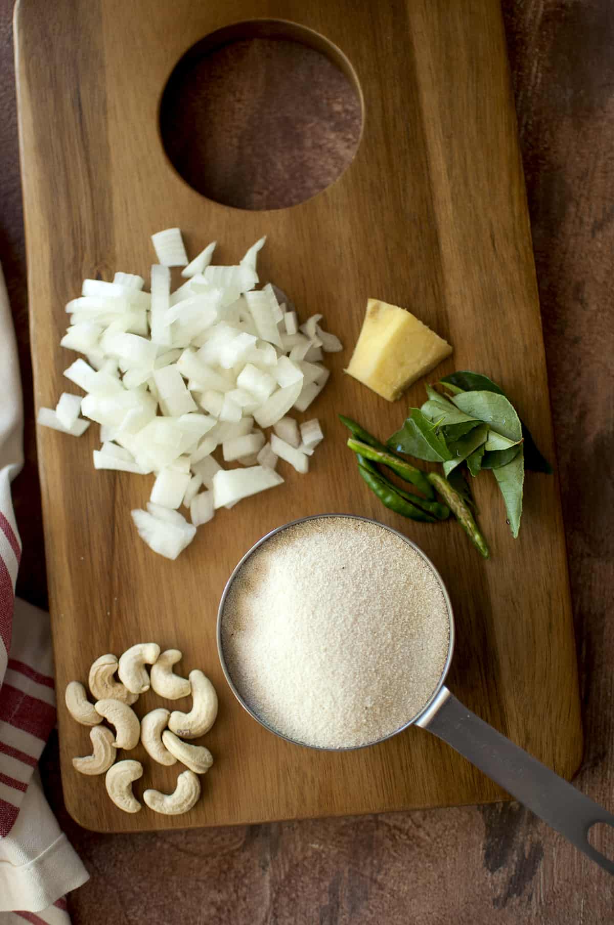 Ingredients for upma on a chopping board - sooji, cashews, chopped onions, ginger, green chilies and curry leaves