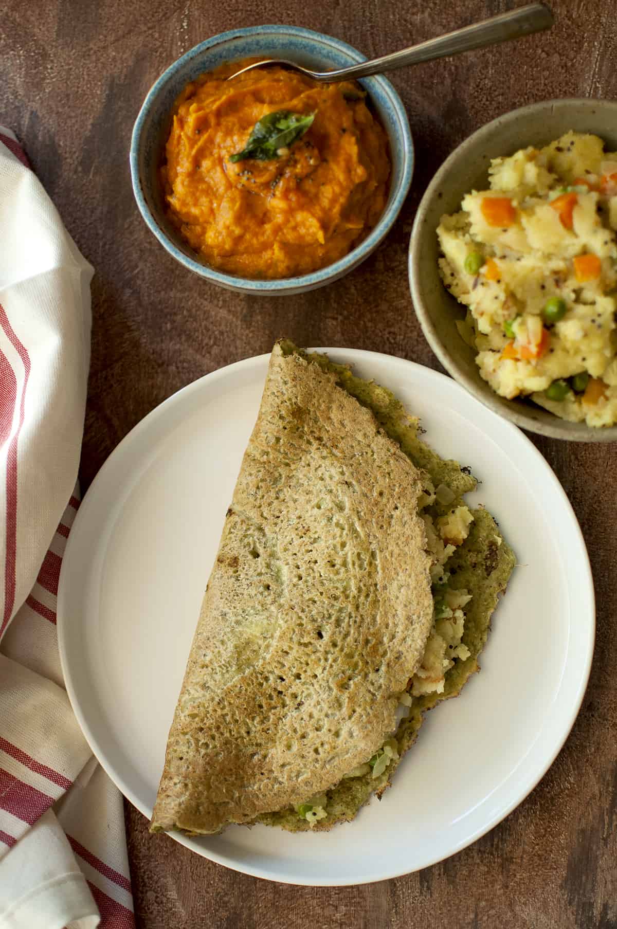 White plate with pesarattu upma with a blue bowl of chutney and bowl of upma