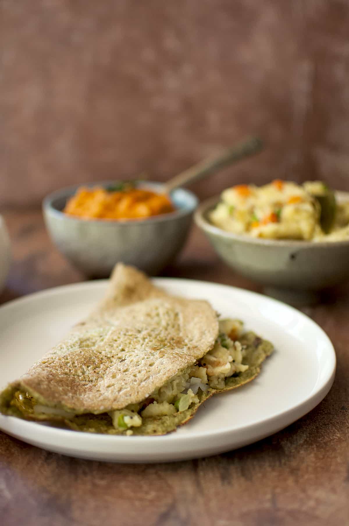 White plate with pesarattu upma with a blue bowl of chutney and bowl of upma