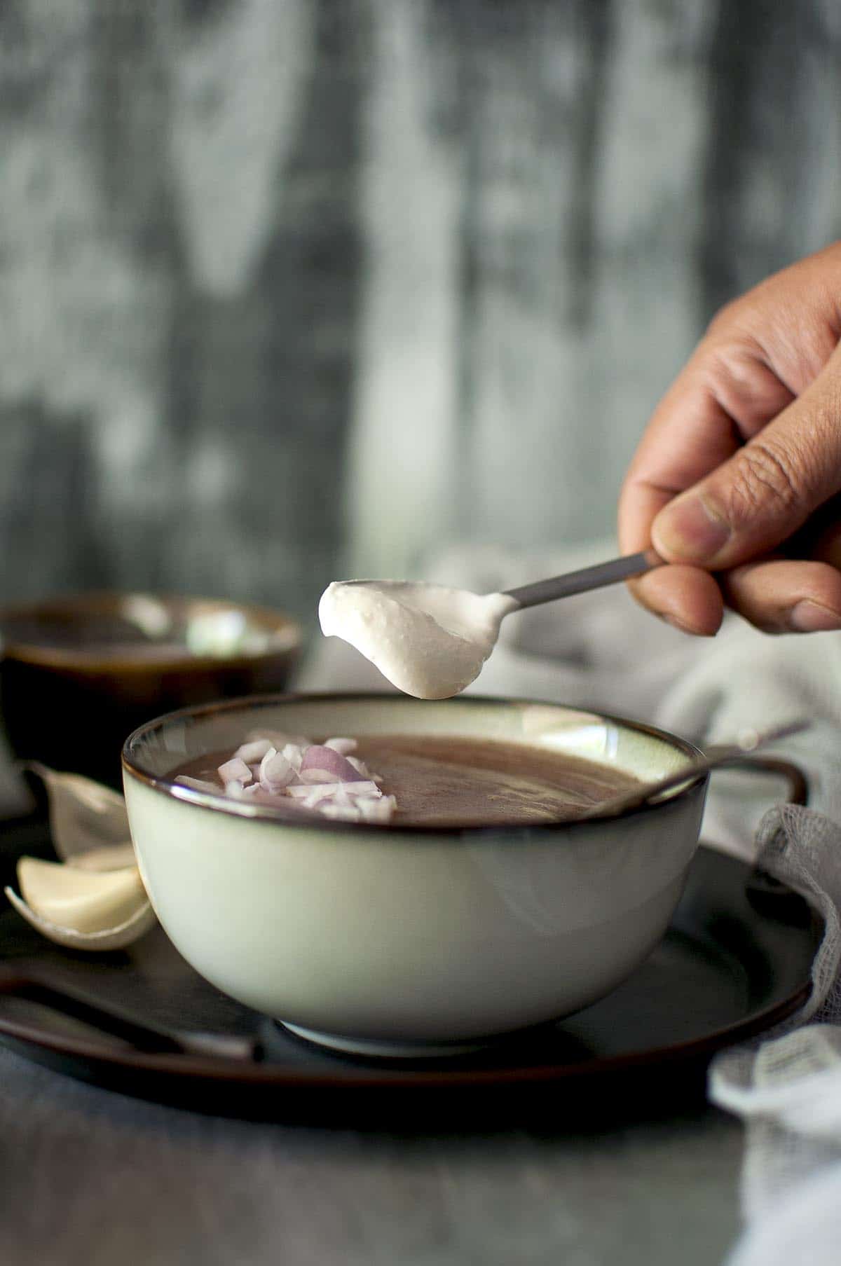 Hand putting a dollop of yogurt into a grey bowl of finger millet soup