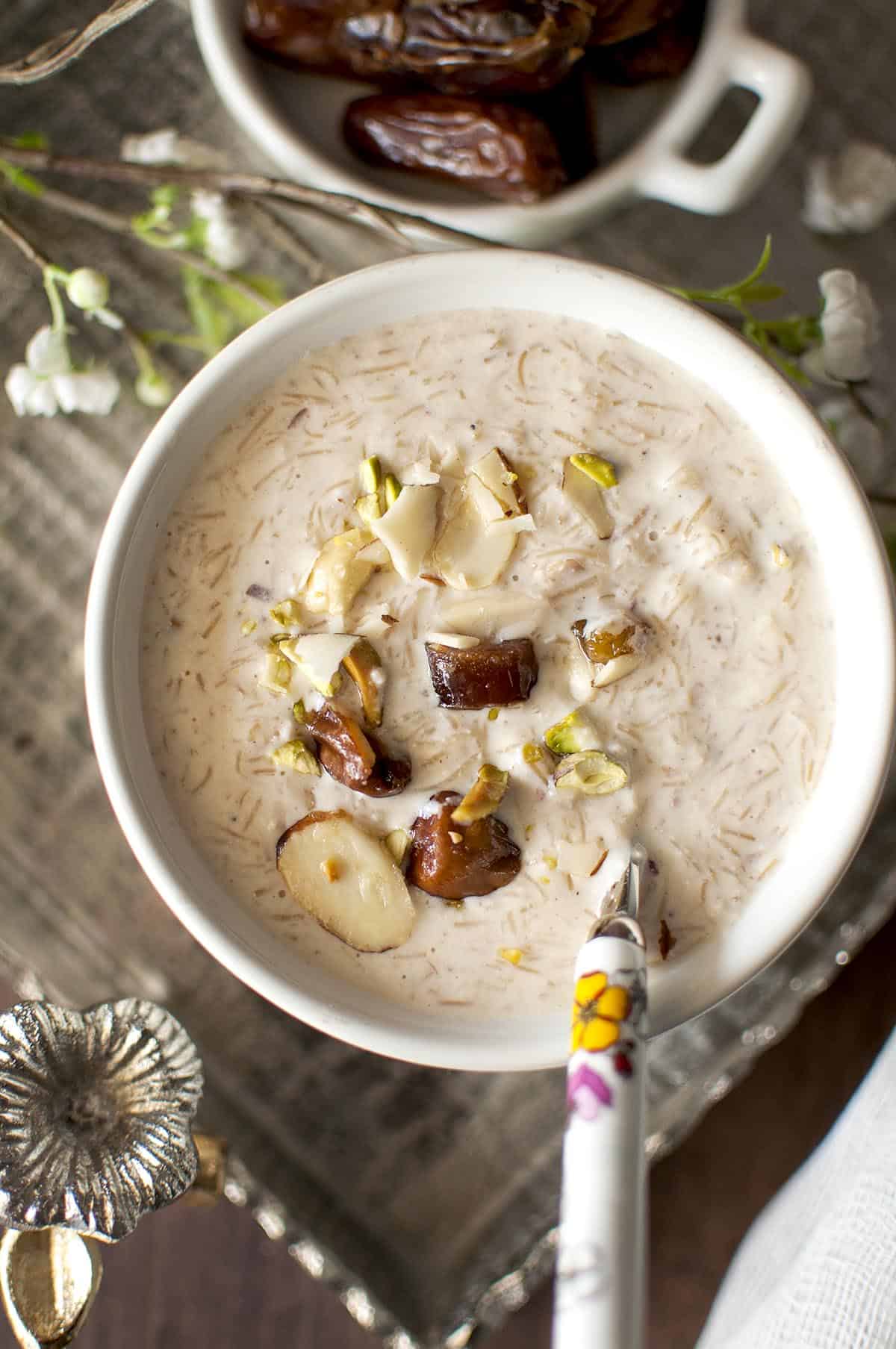 Top view of a white bowl with vermicelli pudding topped with chopped dates and a spoon inside