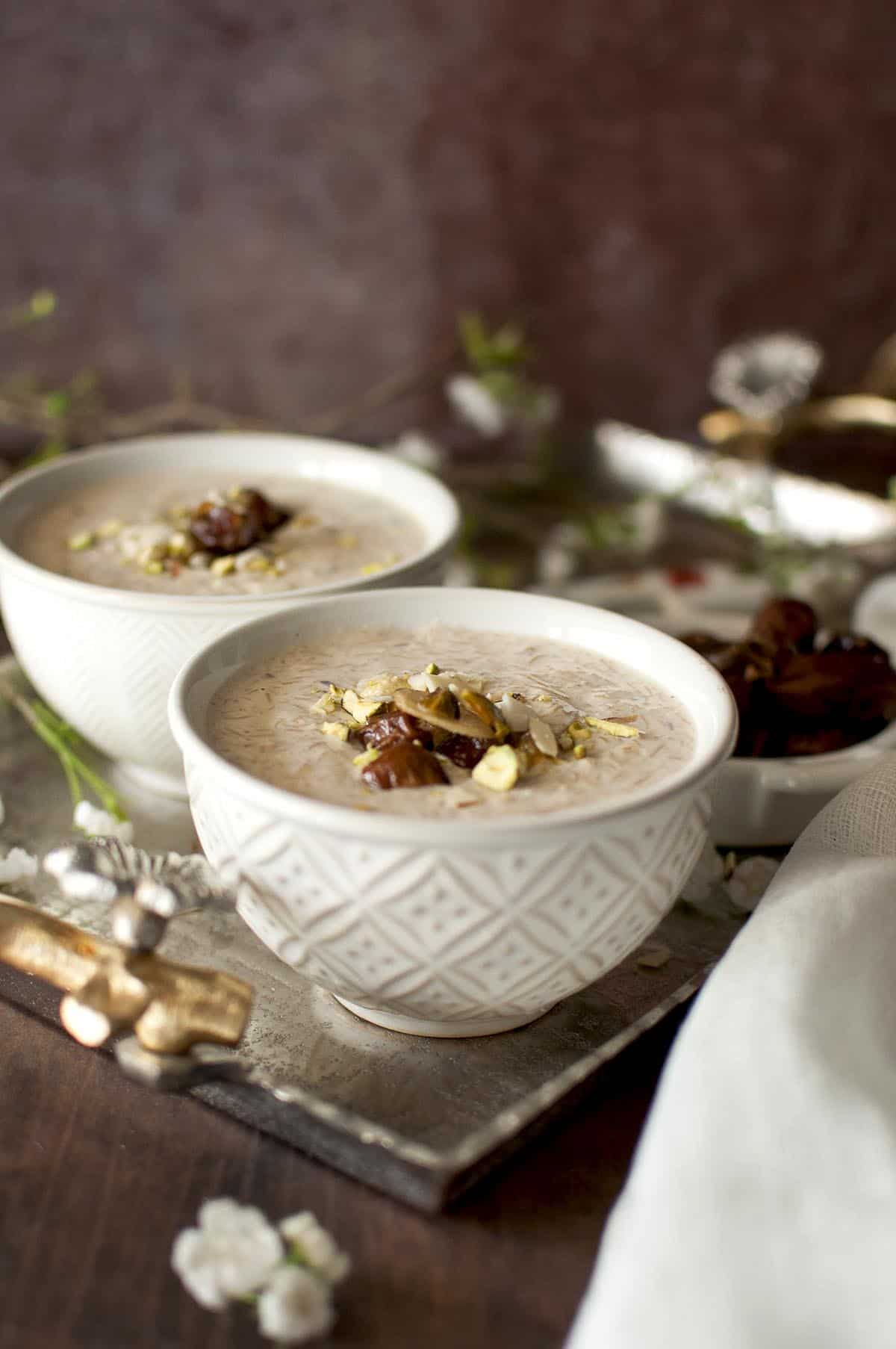 Two cream color bowls with kheer topped with nuts on a silver tray