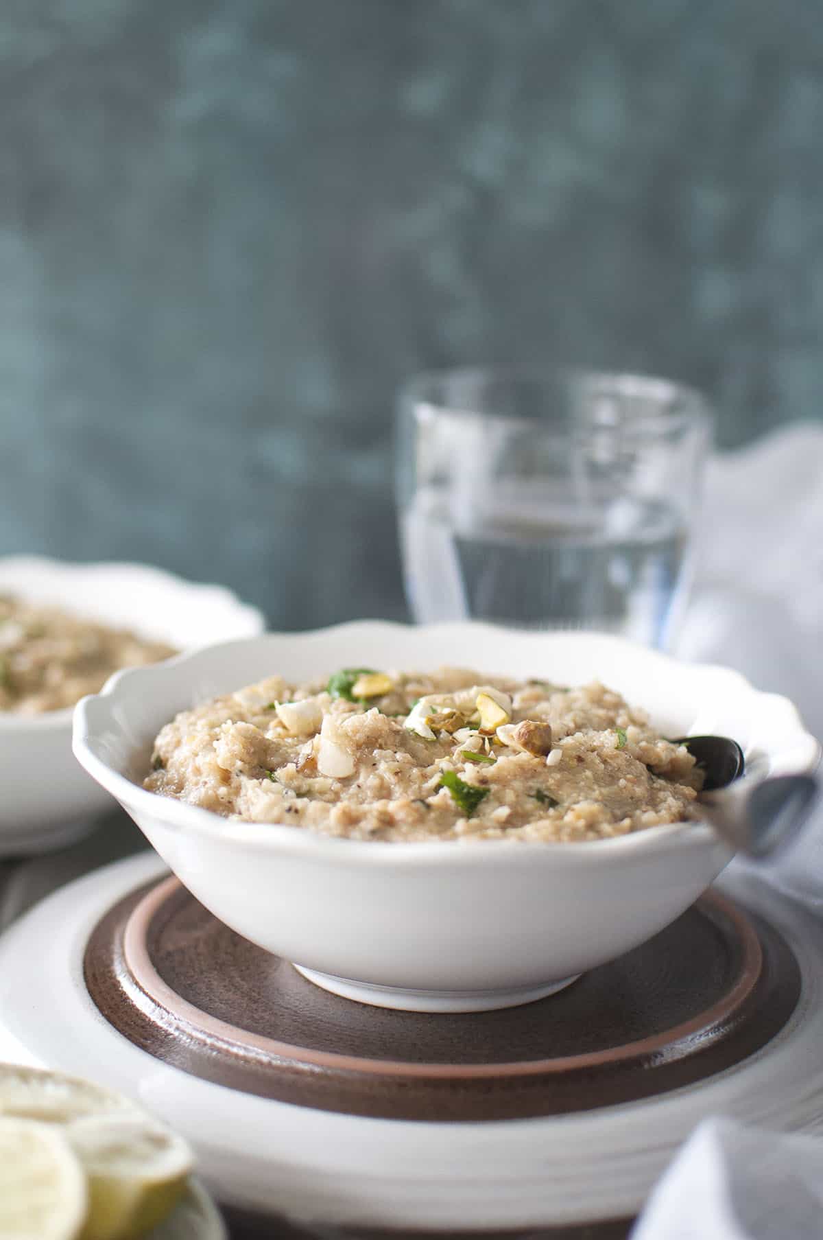 White bowl with Halim and a spoon and a glass of water in the background