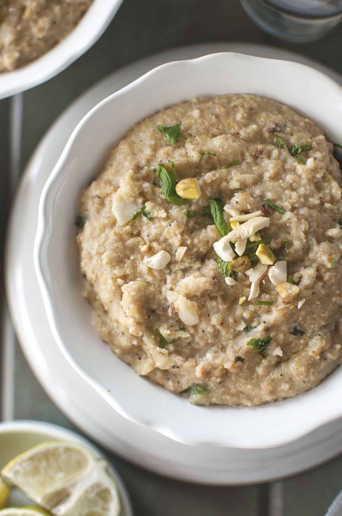 Closeup photo of veg haleem topped with chopped nuts and herbs in a white bowl 