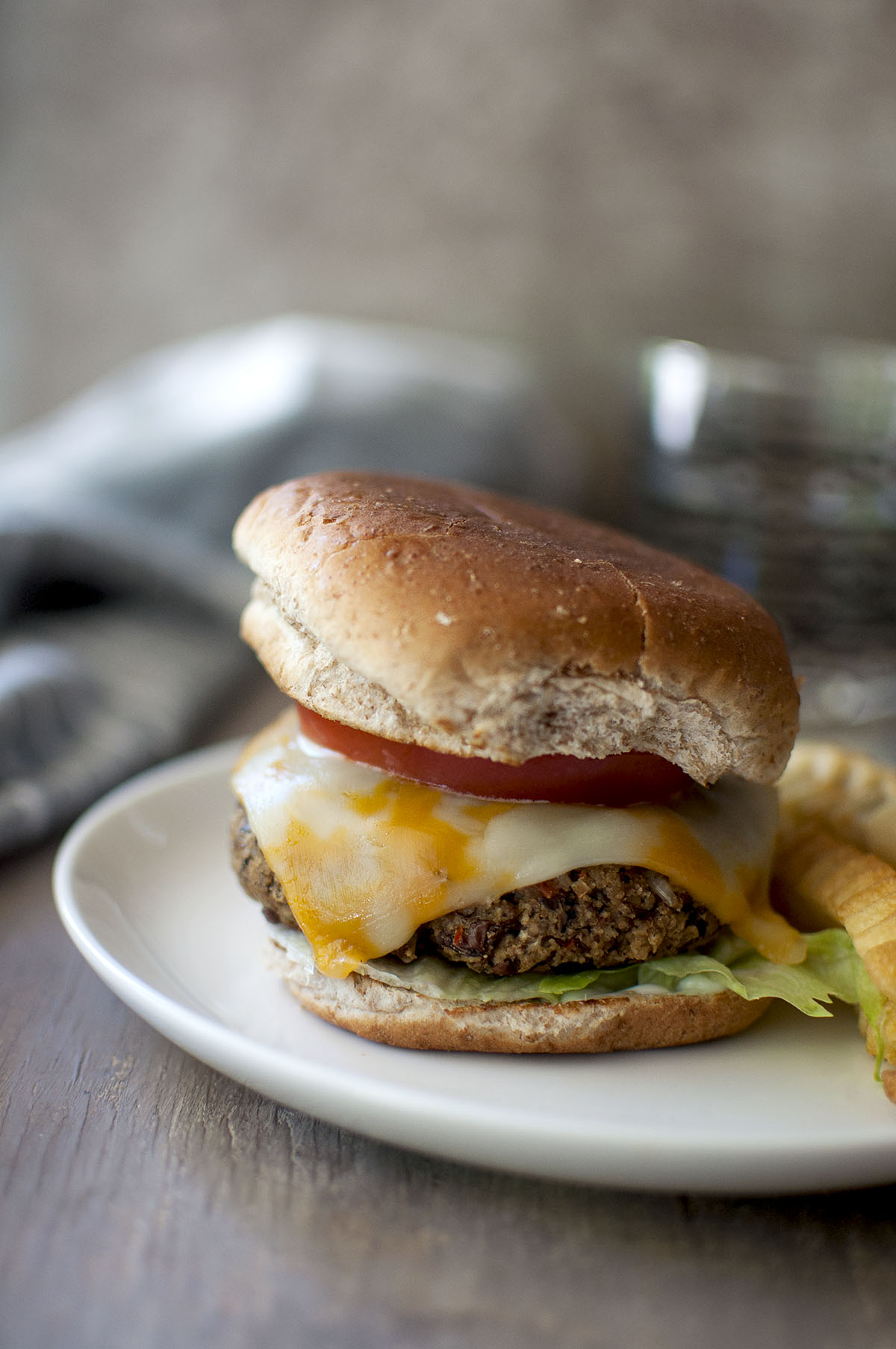 White plate with cheesy adzuki bean burger between buns with lettuce, tomato slice