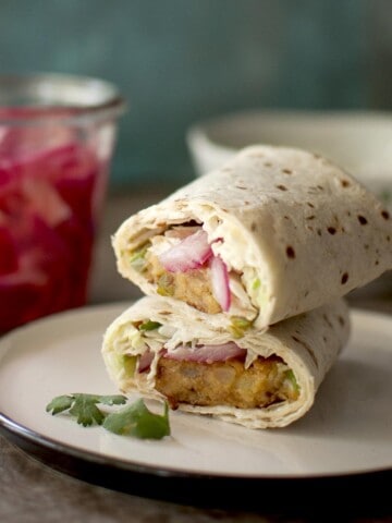 white plate with aloo tikki wrap halves stacked on top of each other