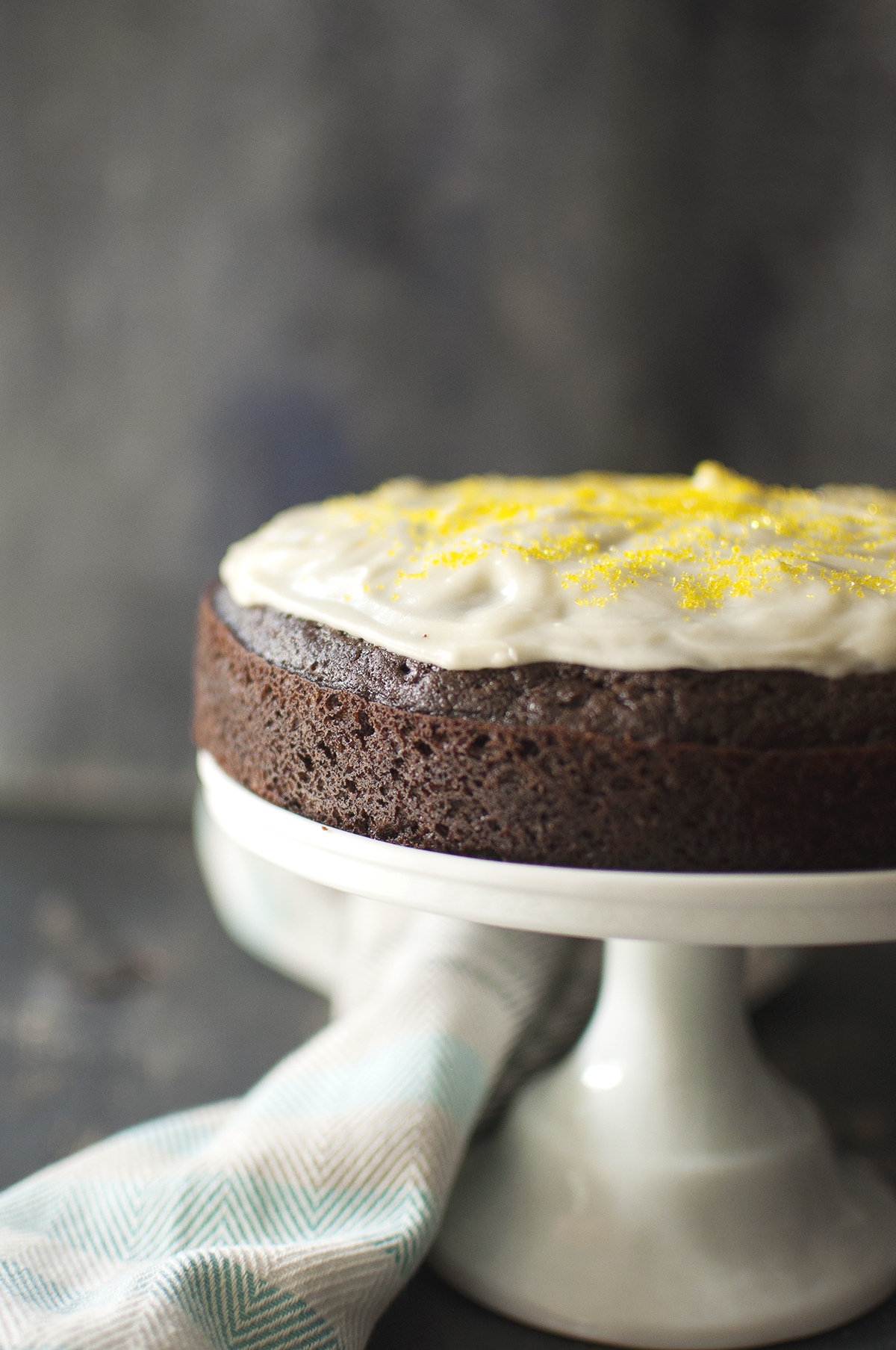 White cake stand with chocolate cake topped with buttercream icing and yellow sprinkles