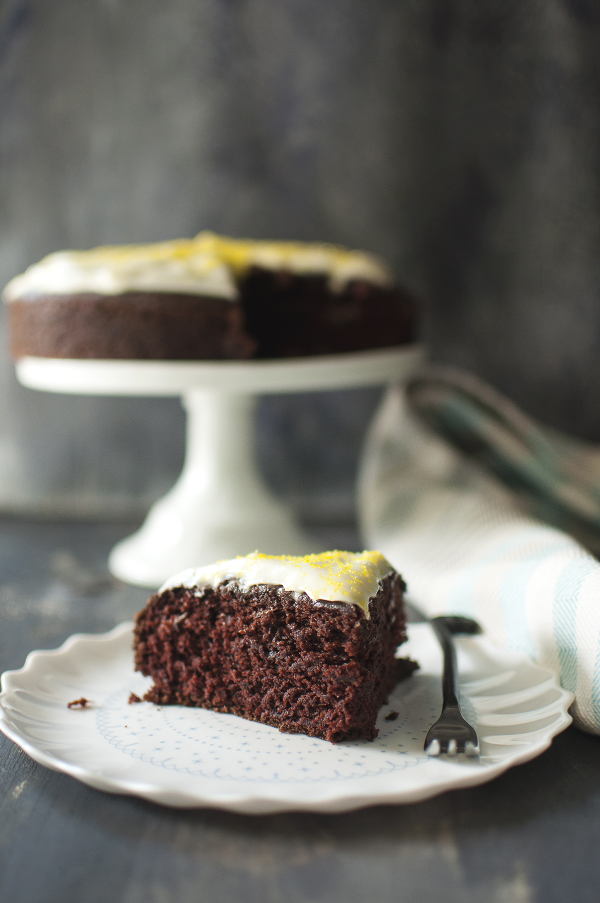 White plate with a slice of cake with a cake stand in the background