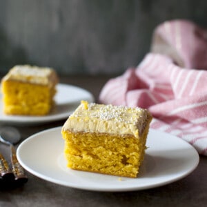 White plate with a square slice of frosted mango cake