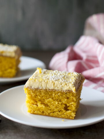 White plate with a square slice of frosted mango cake