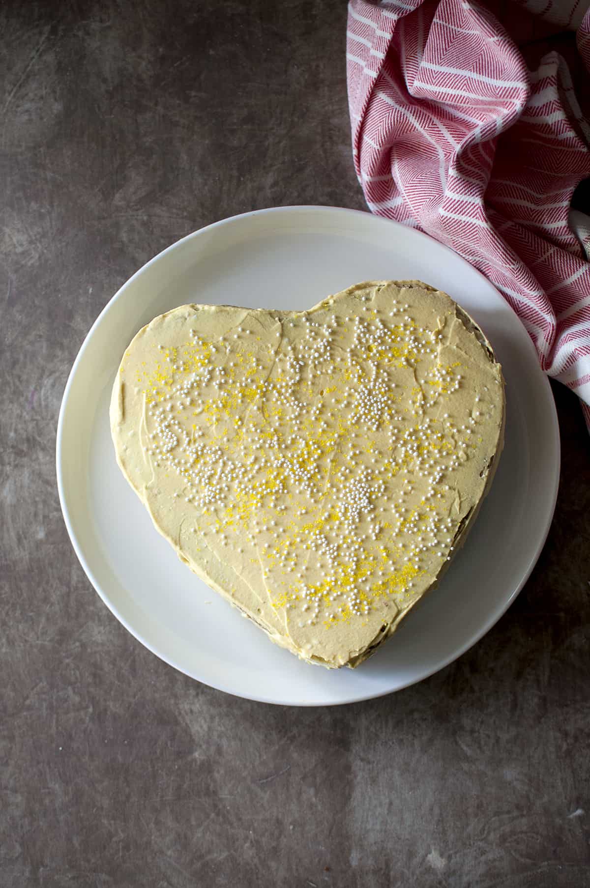 White plate with a heart shaped mango cake with yellow frosting and sprinkles