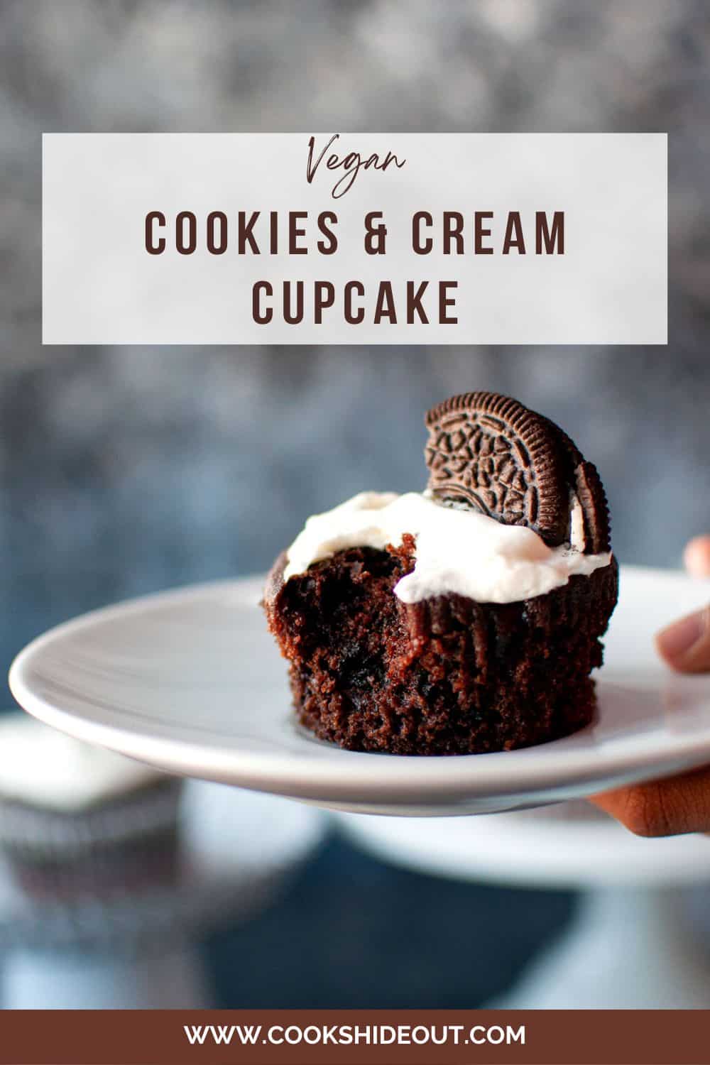 Hand holding white plate with bitten cookies and cream cupcake.