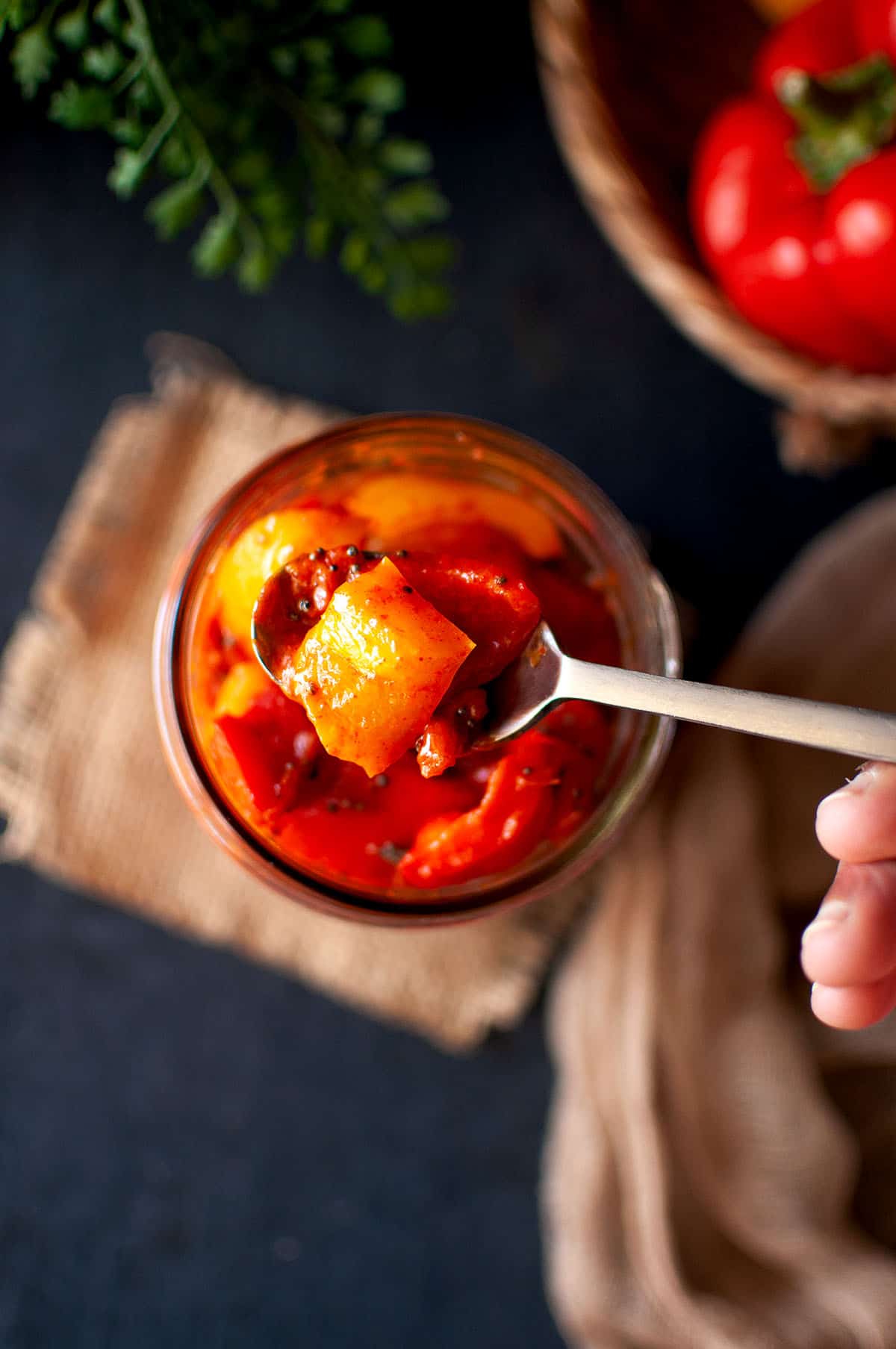 Spoon holding capsicum pickle over mason jar.