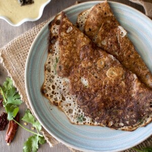 Blue plate with rava dosa with bowls of onion chutney and peanut chutney