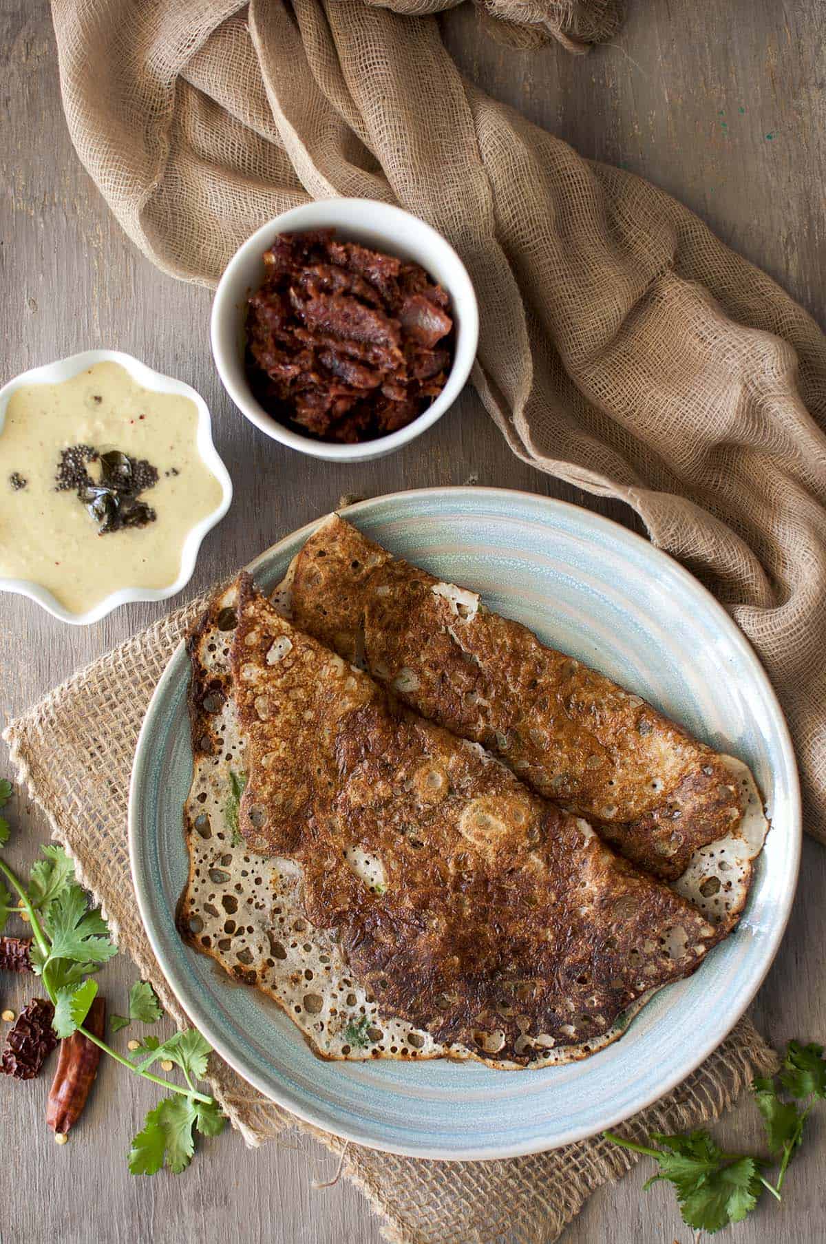 Blue plate with rava dosa with bowls of onion chutney and peanut chutney