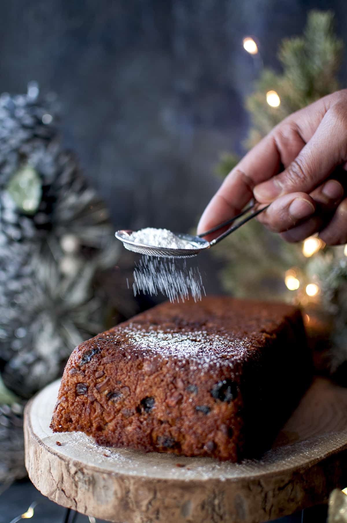 Hand sprinkling powdered sugar on eggless plum cake