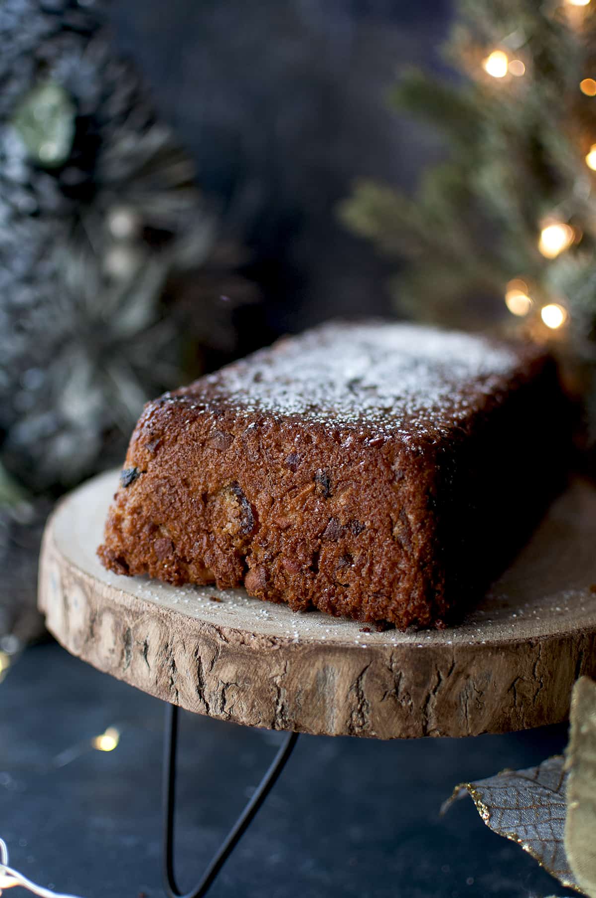 Vegan Fruit cake sprinkled with powdered sugar on a wooden stand