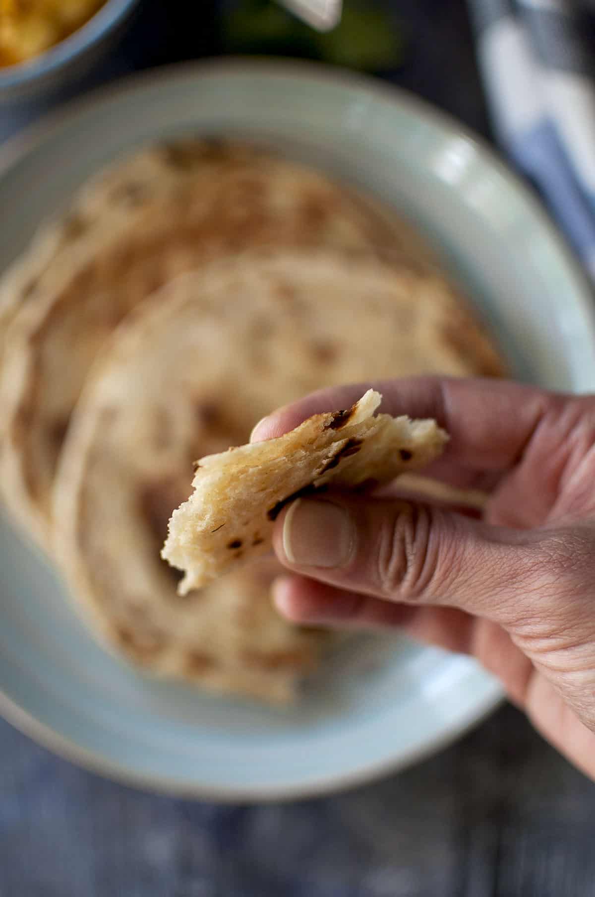 Hand holding a piece of flaky Kerala paratha