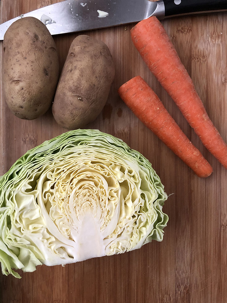 Chopping board with half head of cabbage, 2 carrots and 2 russet potatoes