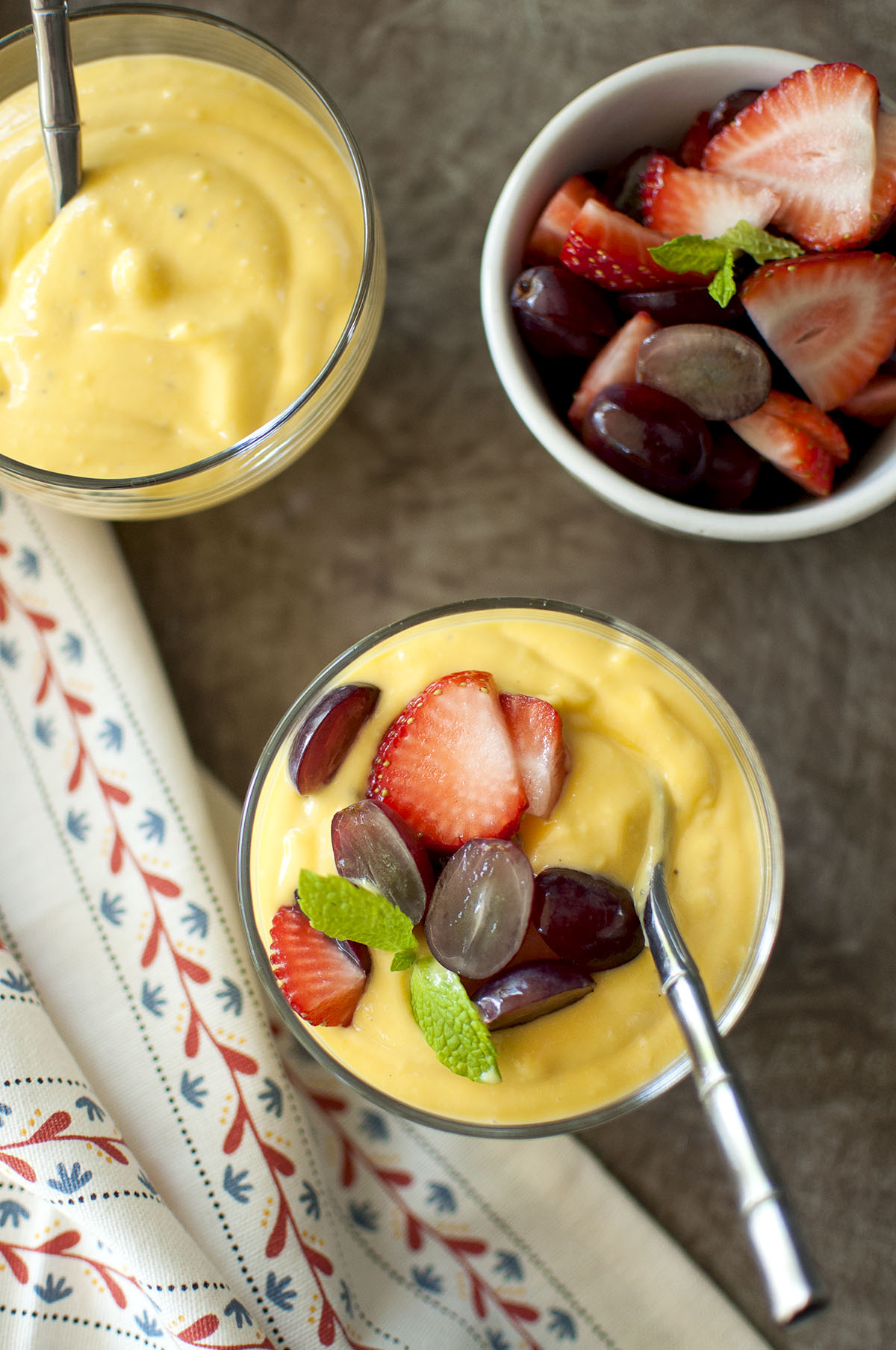 Glass serving cup with fruit custard topped with halved grapes, strawberries and mint sprig.