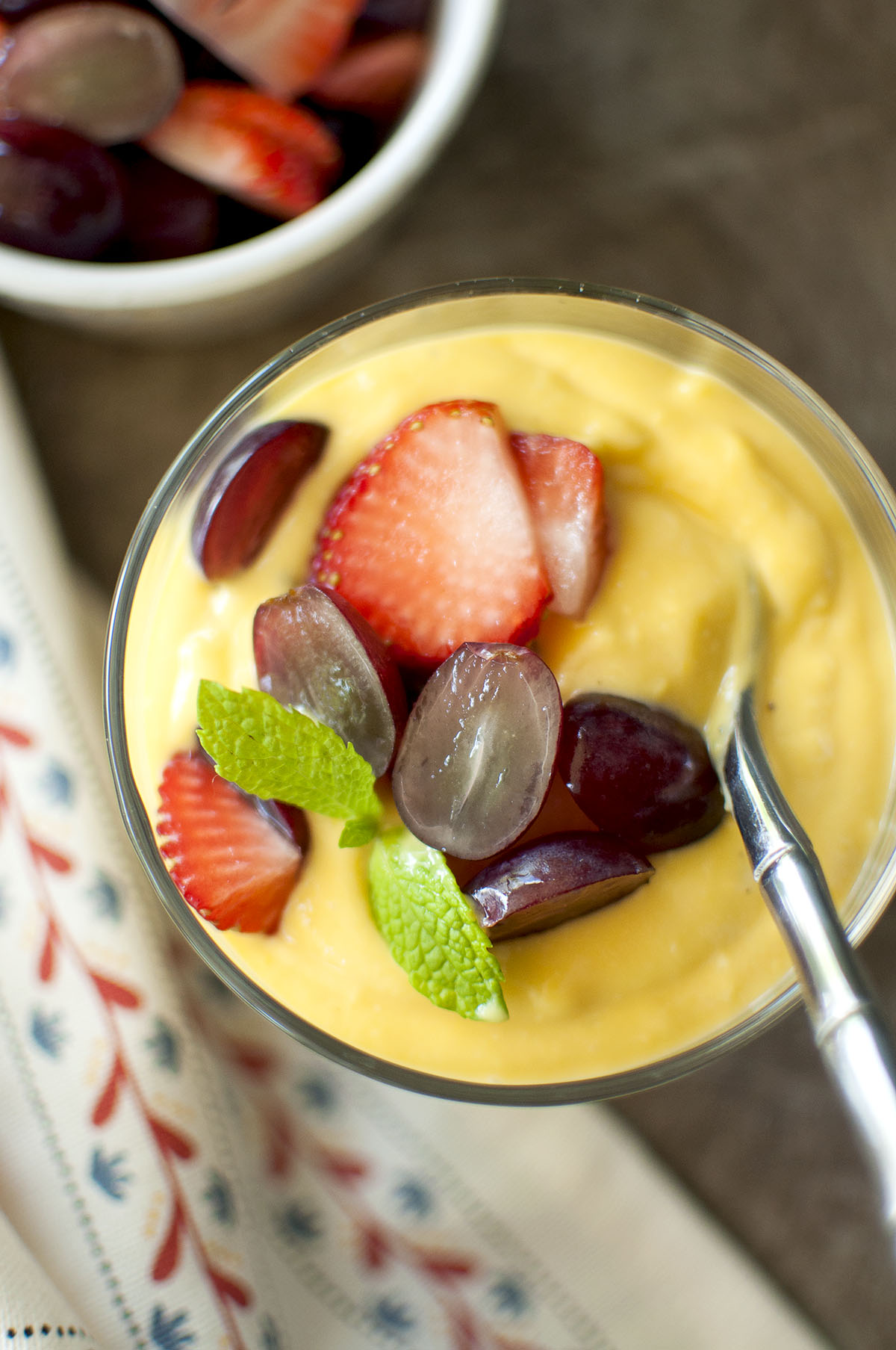 Glass serving bowl with fruit dessert topped with chopped grapes, strawberries and mint.