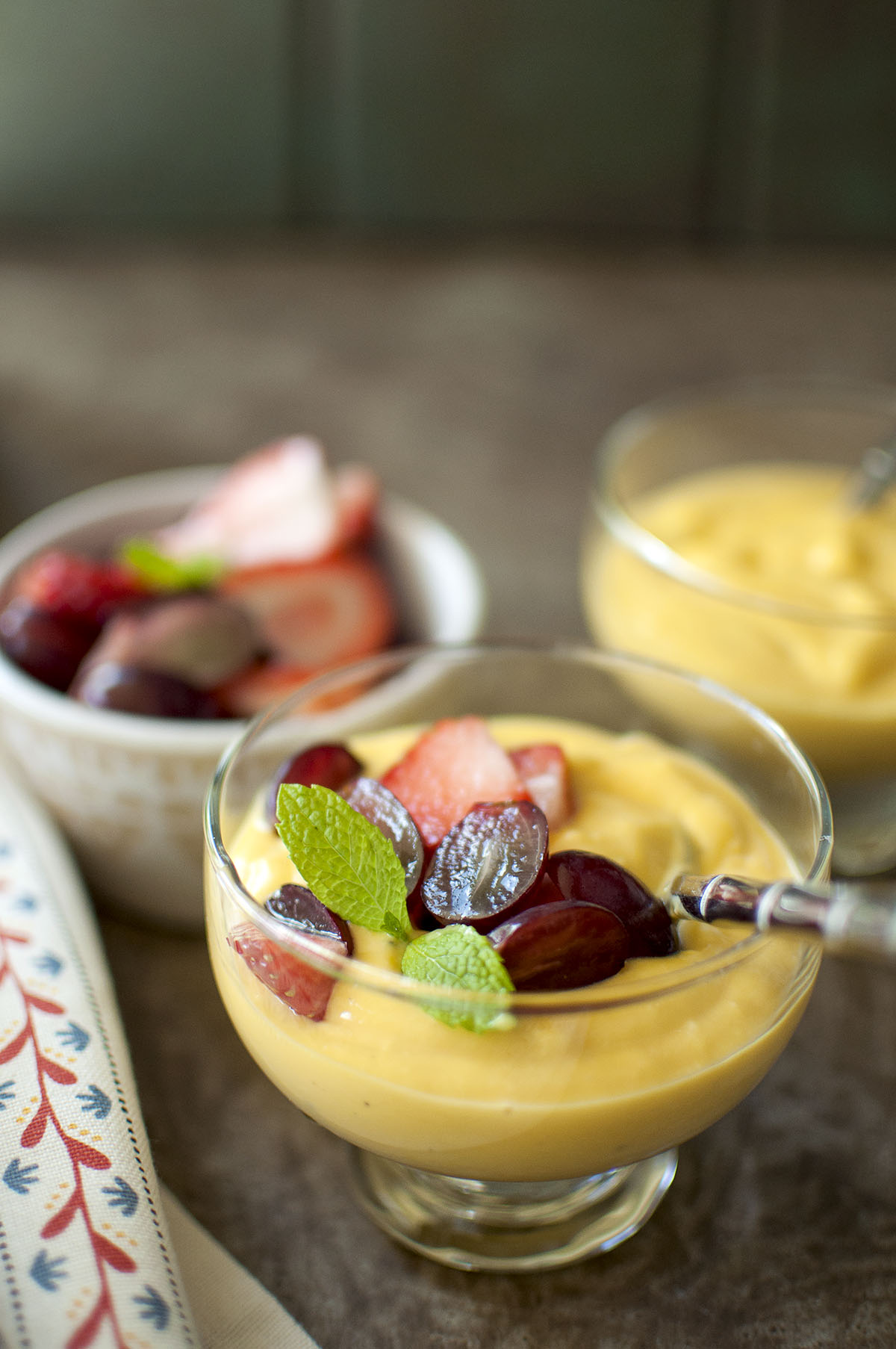 Glass serving cup with fruit custard topped with halved grapes, strawberries and mint sprig.