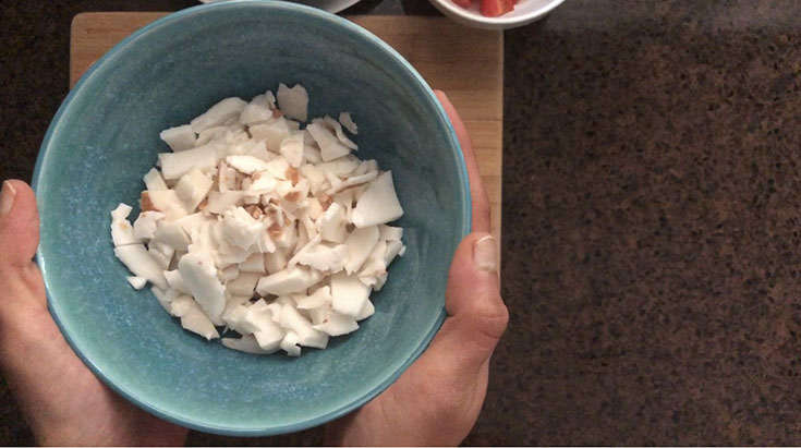 Hands holding a blue bowl with chopped coconut meat