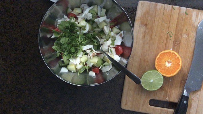 Steel bowl with chopped coconut meat, cucumber, tomatoes, scallions, cilantro and halved lime, orange on the side