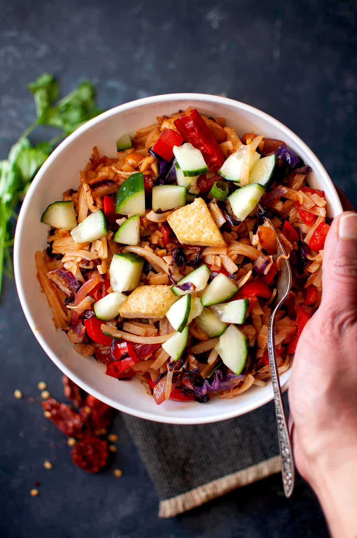 Hand holding white bowl with vegetable Pad Thai.