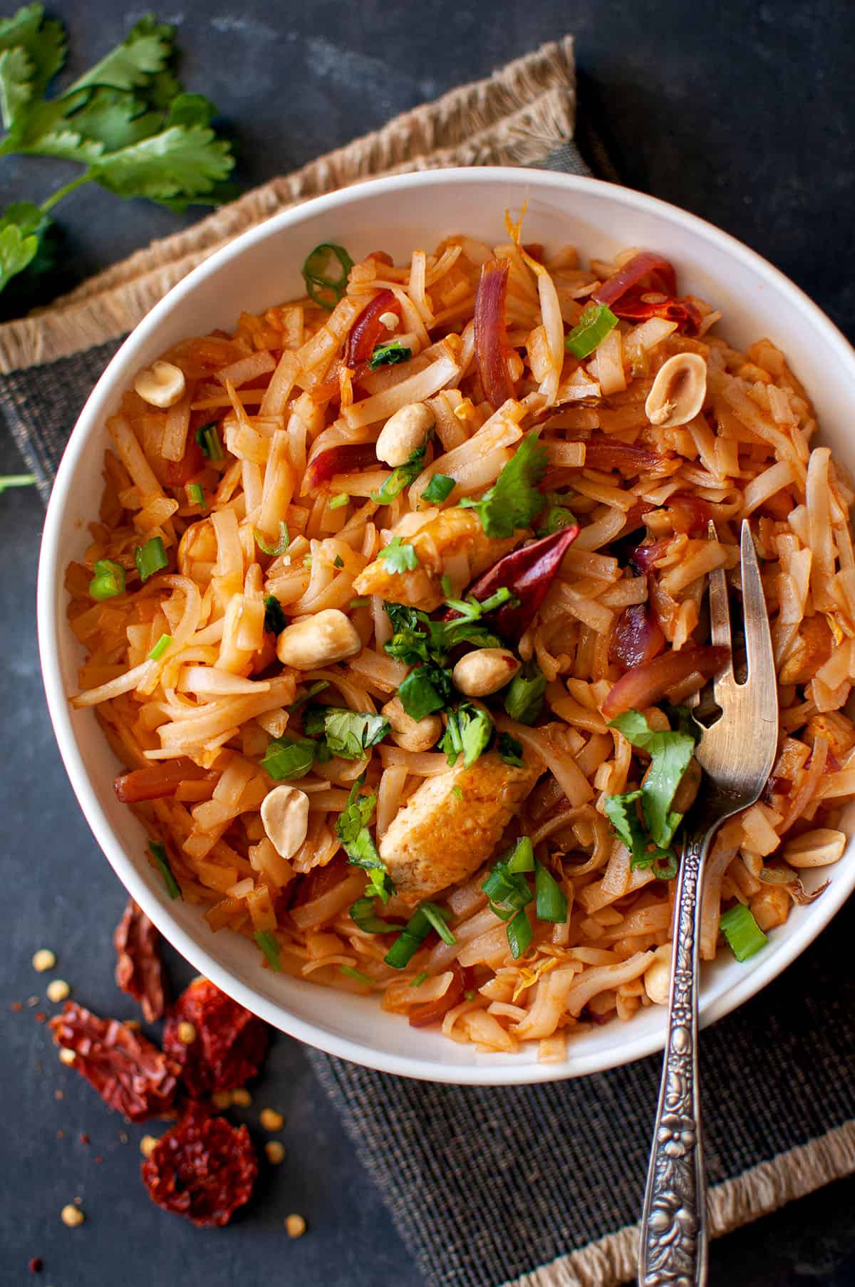 White bowl with vegan pad thai noodles with a fork inside.