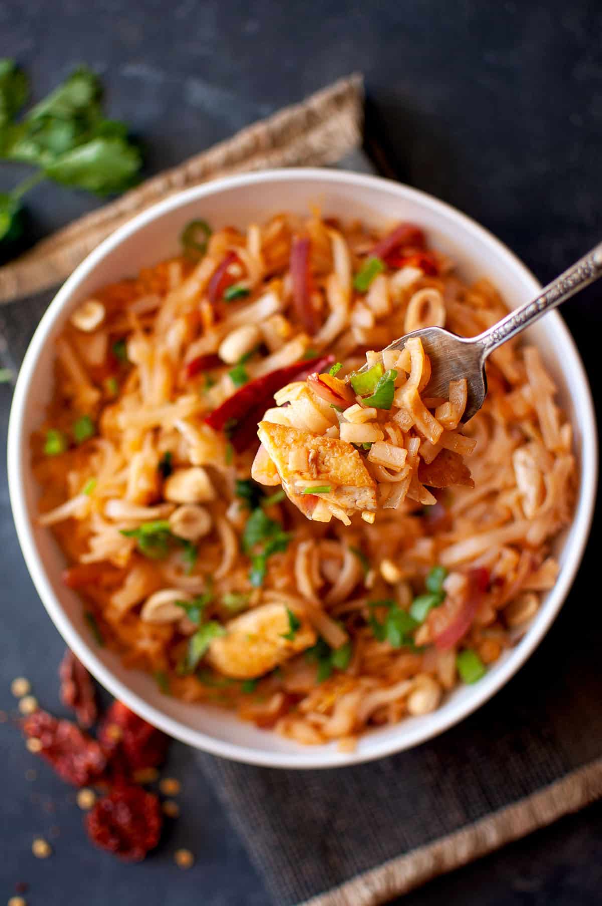 Fork with wide rice noodle stir fry over a bowl of Pad thai.