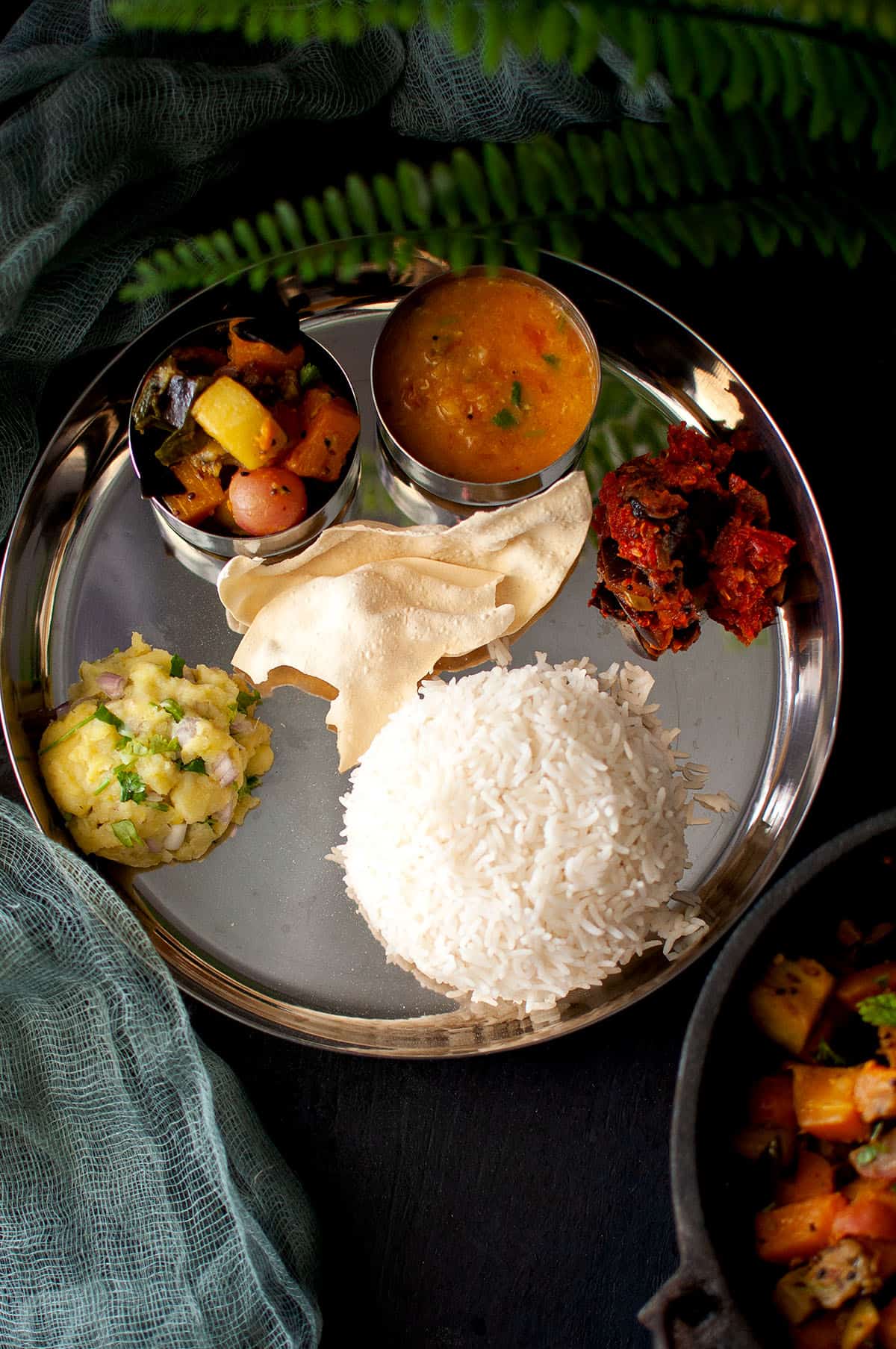 Steel plate with rice, curry, dal, aloo pitha and papad.