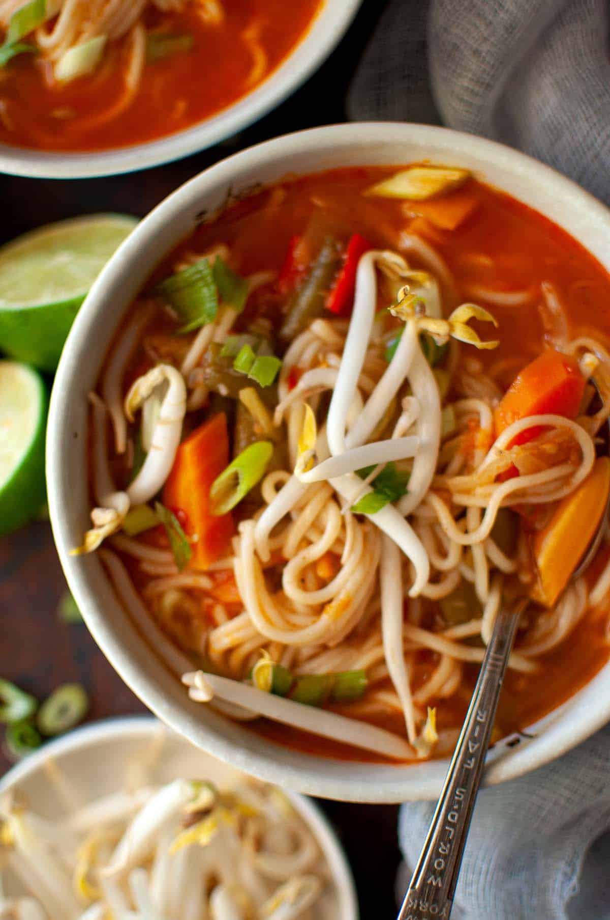 White bowl with veg noodle soup topped with bean sprouts