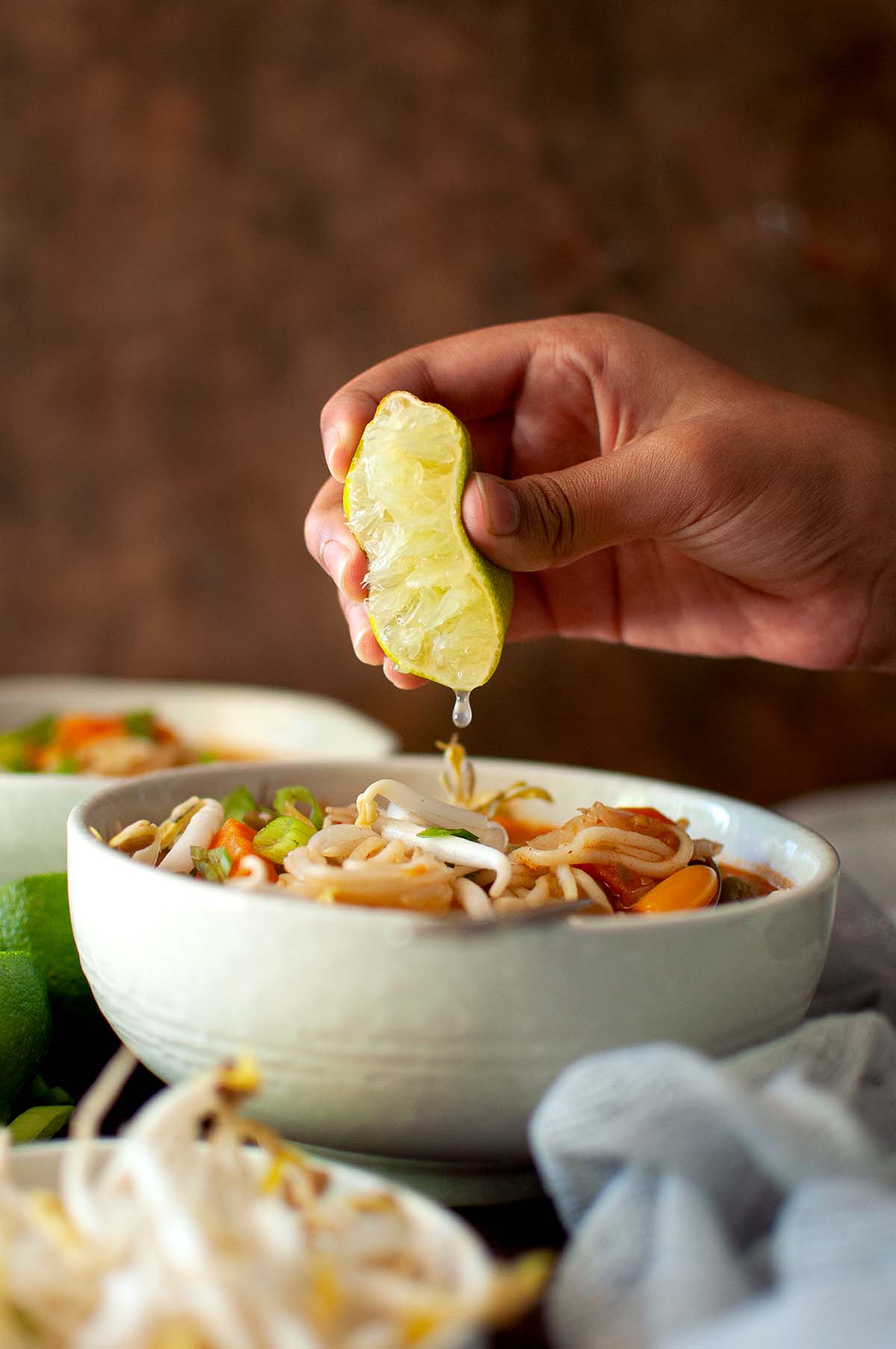 Hand drizzling lemon juice onto a bowl of noodle soup