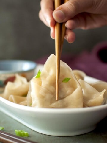 Hand holding vegetarian momos with chopsticks