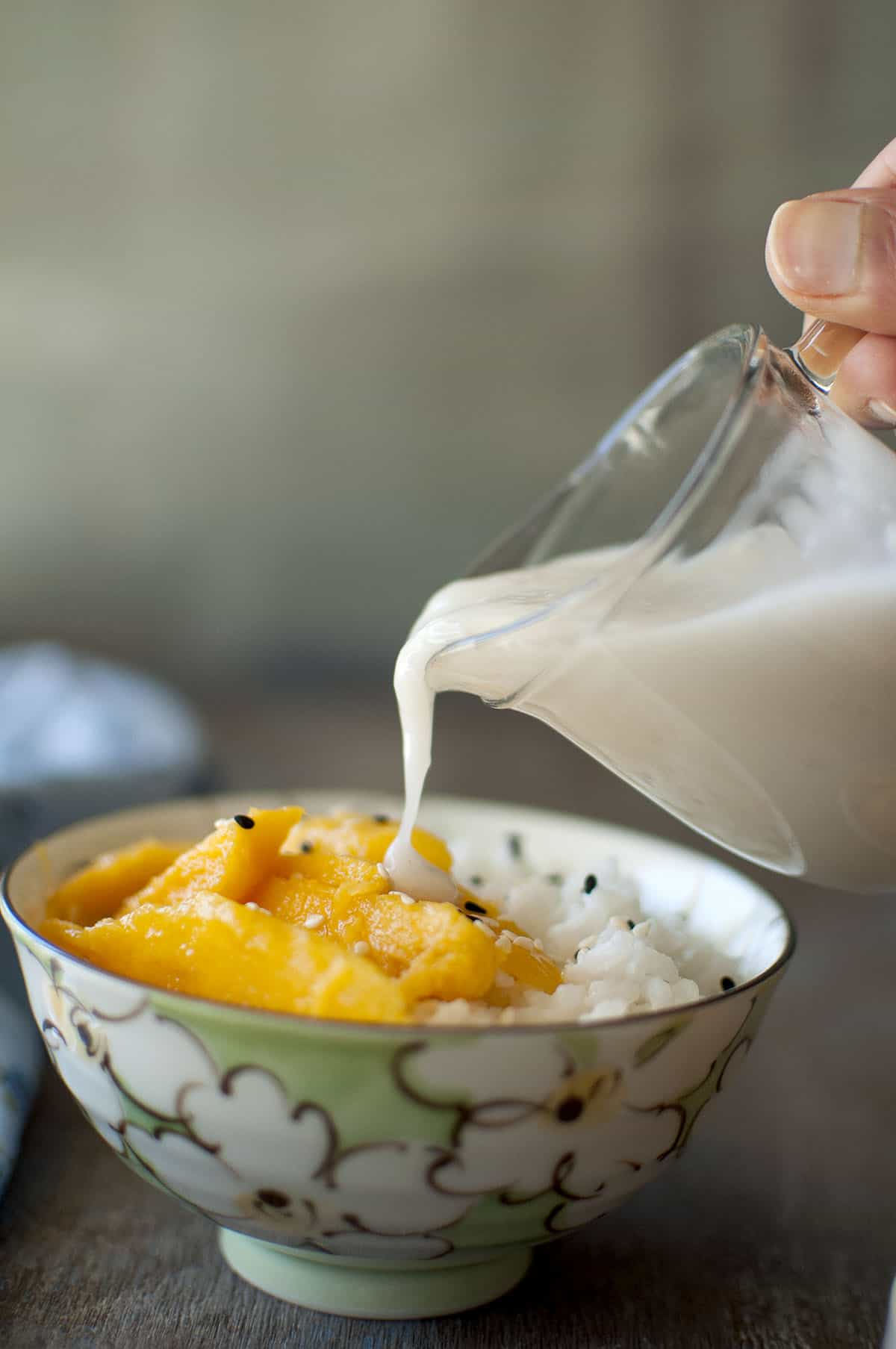 Hand pouring coconut sauce on mango and rice in a bowl