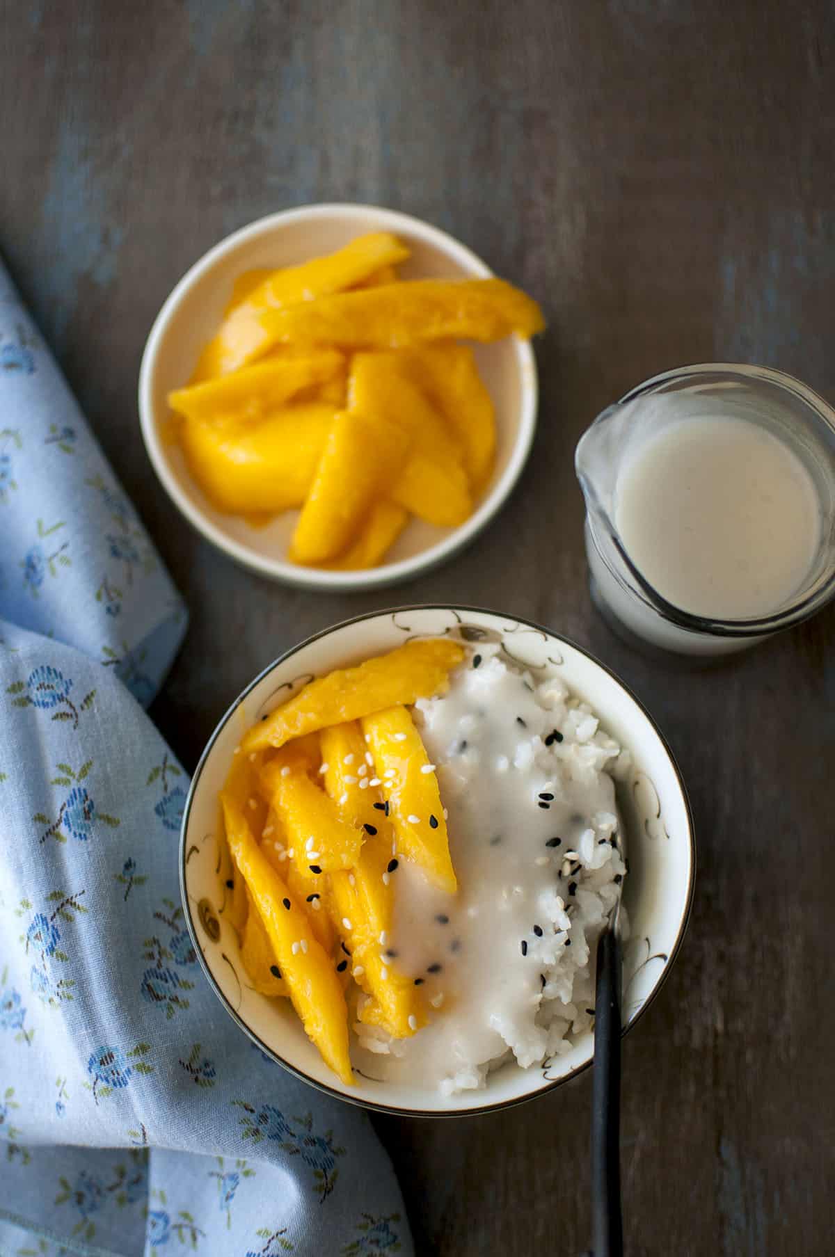 White Bowl with sticky rice and chopped mangoes topped with sesame seeds and sweet coconut sauce