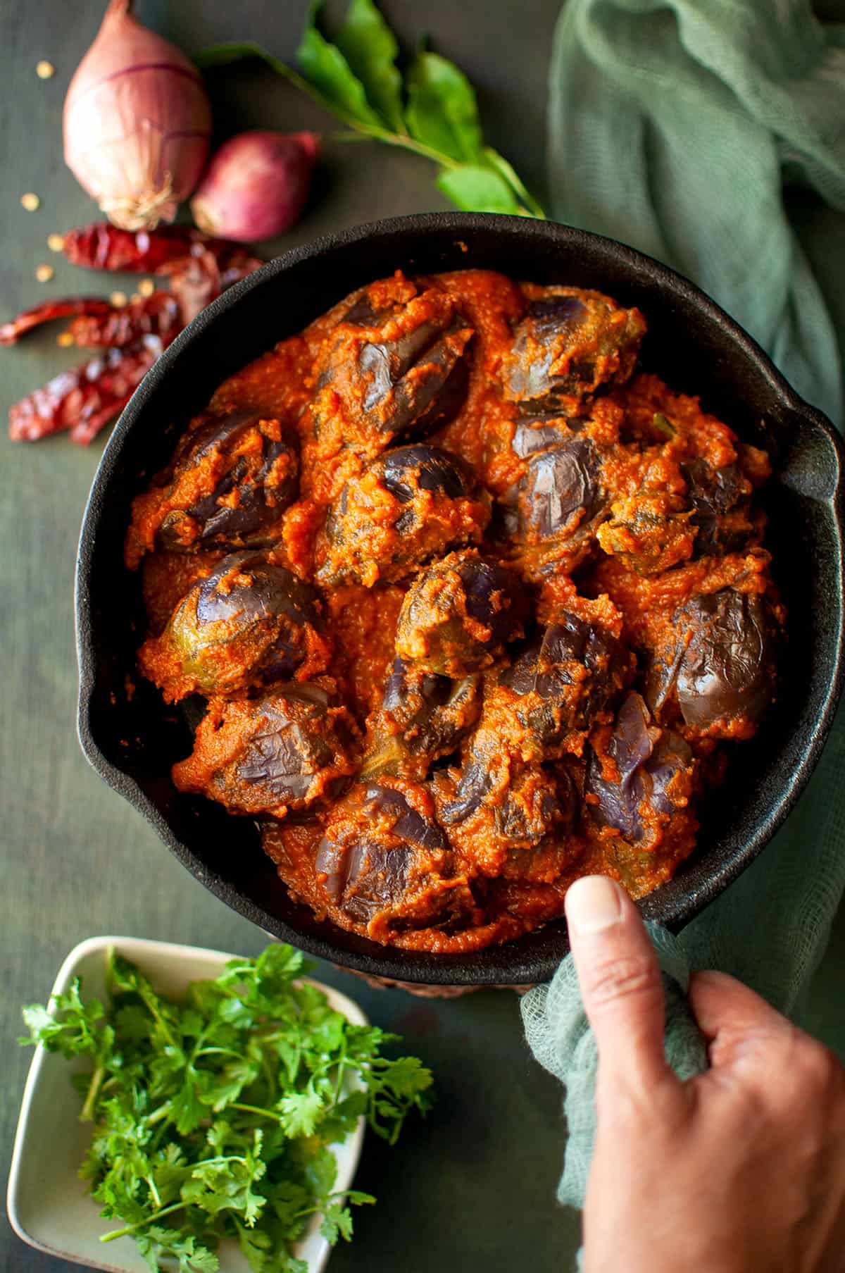 Hand holding a cast iron pan with vankaya masala kura.