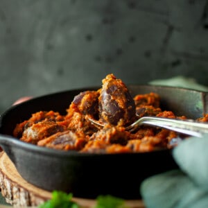 Spoon with baby eggplant in a cast iron pan.