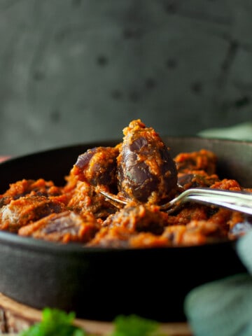 Spoon with baby eggplant in a cast iron pan.