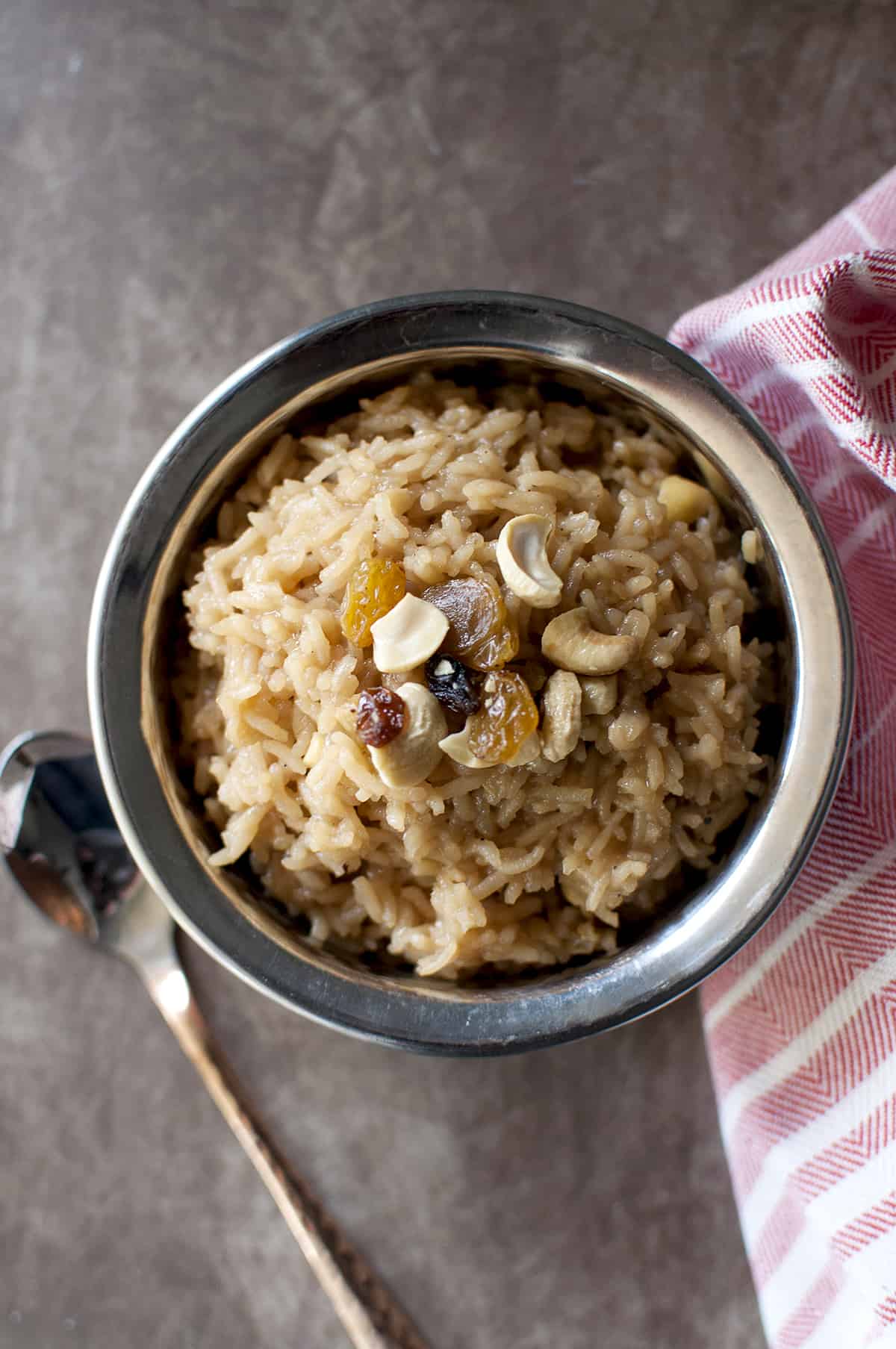 Steel bowl with rice pudding topped with cashews and raisins