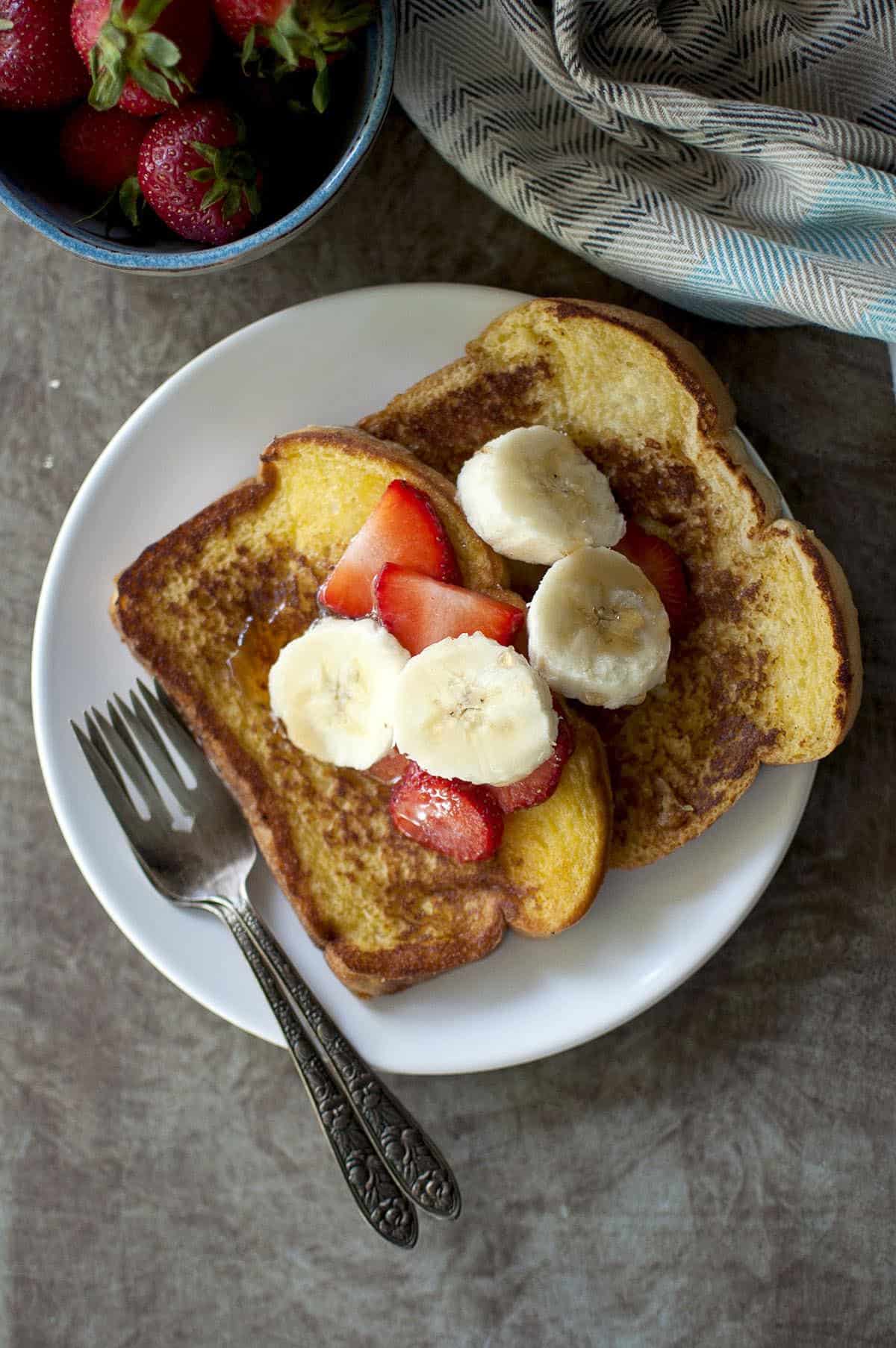 white plate with 2 slices of french toast topped with fresh fruit