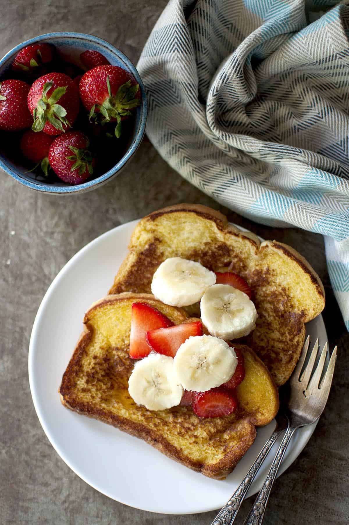 White plate with 2 french toast slices topped with fresh fruit