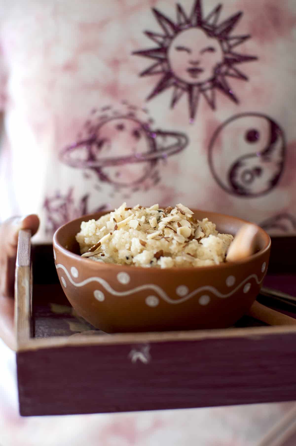 Hand holding a burgundy tray with a bowl of sooji halwa
