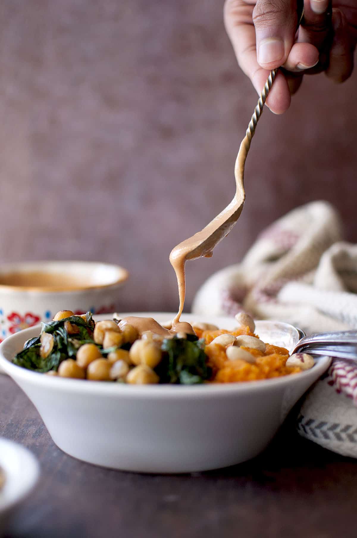 White bowl with mashed sweet potatoes and a hand pouring peanut sauce on it