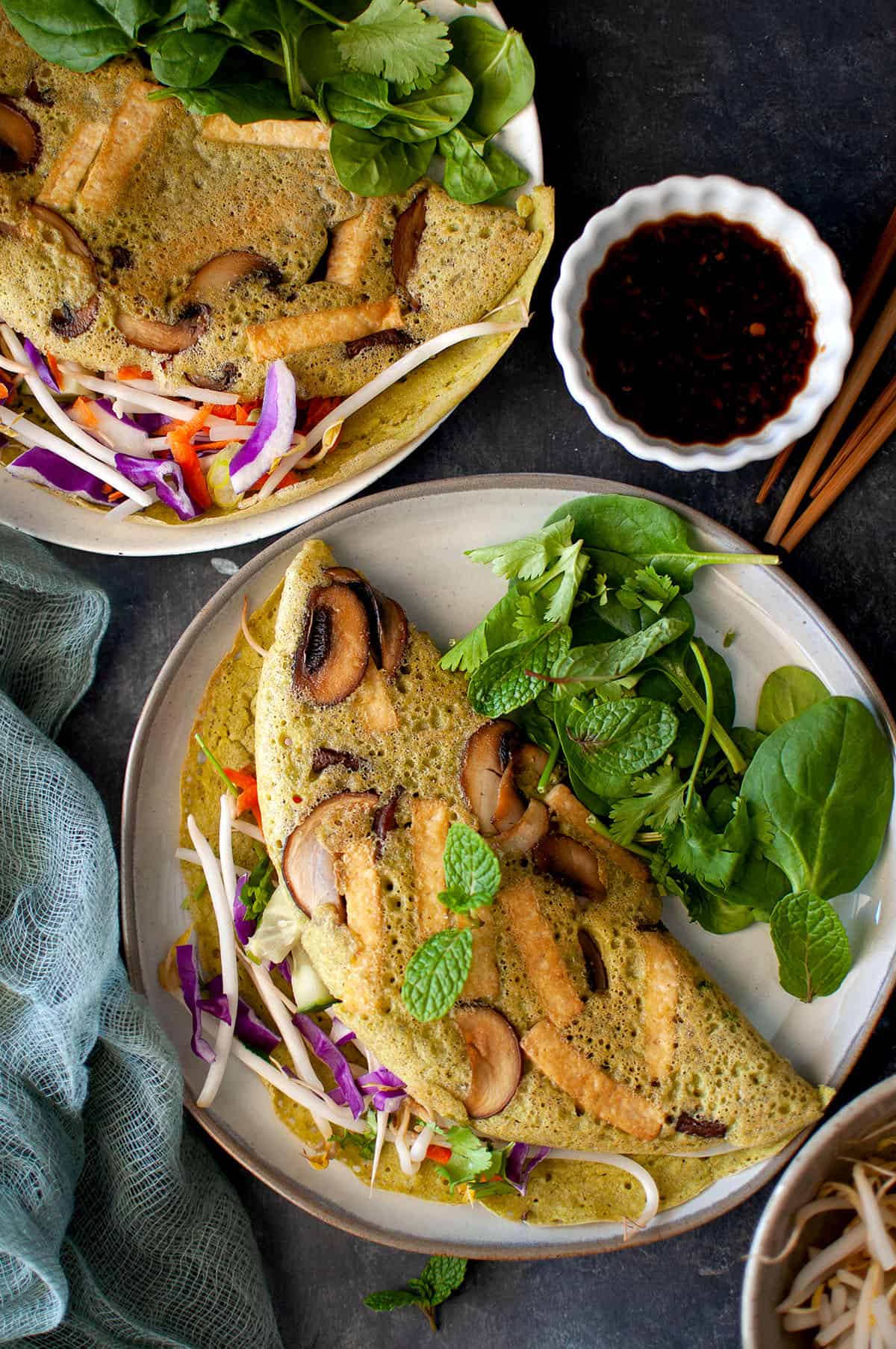 Grey plate with Vegan banh xeo topped with fresh herbs.